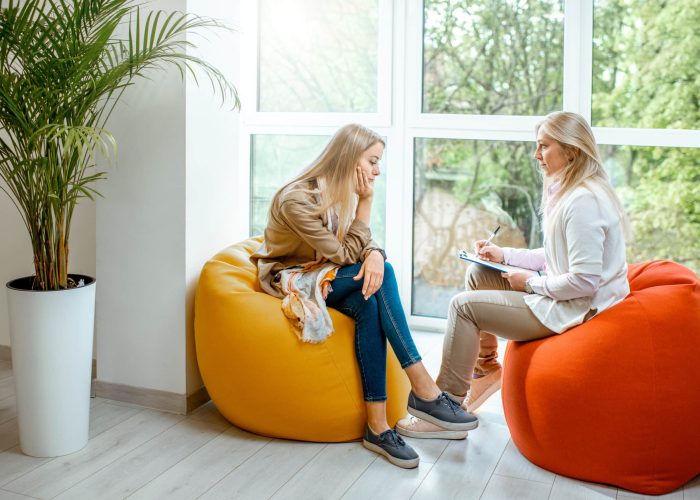 Young woman with senior female psychologist or mental coach sitting on the comfortable chairs during the psychological counseling in the office